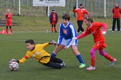 Nachhaltige Szene eines Fu&szlig;ballspiels: Ein Torwart in Gelb springt, w&auml;hrend Spieler in Rot und Blau, in Aktion, agieren.