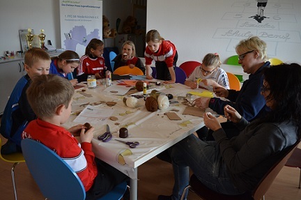 Gruppe von Kindern und Erwachsenen beim Basteln an einem Tisch, umgeben von Bastelmaterialien und Werkzeugen.
