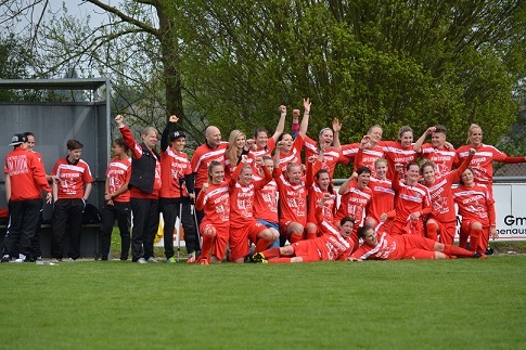 Feiernde Frauenfu&szlig;ballmannschaft in roten Trikots posiert auf dem Rasen, einige Heben die Arme freudig hoch.