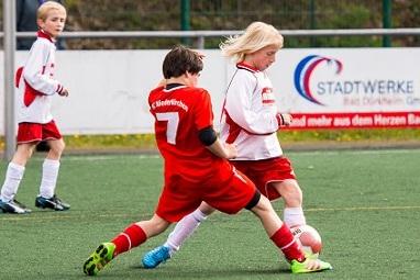Zwei Kinder im Fußballspiel: Ein Junge im roten Trikot foult einen anderen Jungen im weißen Trikot am Ball.