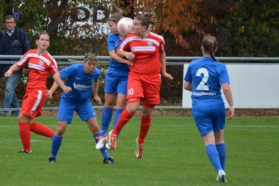 Zwei Fu&szlig;ballspielerinnen springen um den Ball, w&auml;hrend zwei weitere Spielerinnen in blauen Trikots in der N&auml;he stehen.