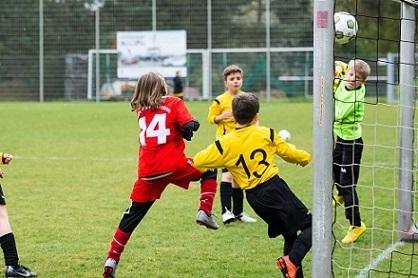 Zwei Kinder im Fu&szlig;ballspiel, ein Spieler in Rot schie&szlig;t, w&auml;hrend der Torwart in Gelb den Ball abwehrt.