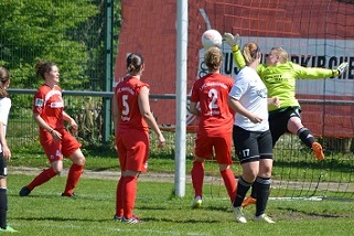 Torwartin springt hoch, um einen Ball w&auml;hrend eines Frauenfu&szlig;ballspiels zu halten, w&auml;hrend Spielerinnen zuschauen.