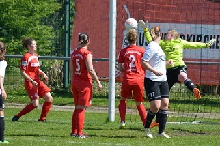 Torwartin springt hoch, um einen Ball w&auml;hrend eines Frauenfu&szlig;ballspiels zu halten, w&auml;hrend Spielerinnen zuschauen.
