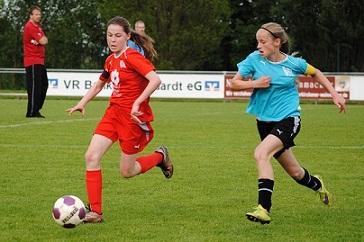 Zwei M&auml;dchen spielen Fu&szlig;ball auf einem gr&uuml;nen Feld, eines in rotem, das andere in blauem Trikot.