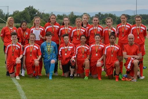 Gruppe von Fu&szlig;ballspielern in roten Trikots mit Medaillen, posierend auf einem Sportplatz im Freien.