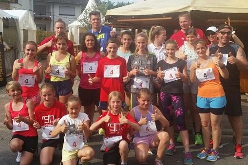 Gruppe von L&auml;ufern in Sportkleidung mit Nummern auf Brust, posiert fr&ouml;hlich im Freien nach einem Event.