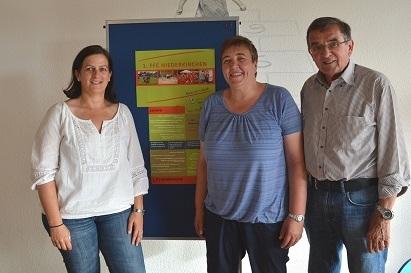 Drei Personen stehen vor einem Plakat des 3. FFC Niederrieden, l&auml;cheln und posieren in einem hellen Raum.