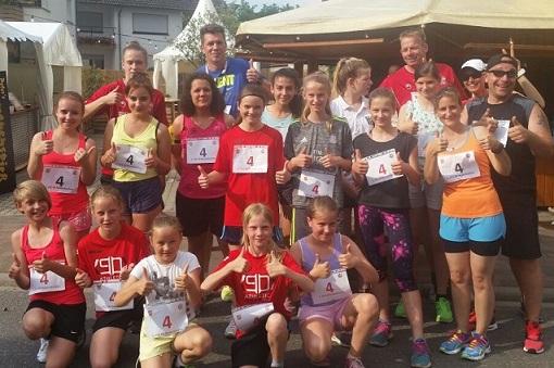 Gruppe von L&auml;ufern in Sportkleidung mit Nummern auf Brust, posiert fr&ouml;hlich im Freien nach einem Event.