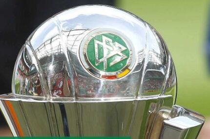 Nahaufnahme eines silbernen Pokals mit dem DFB-Logo auf einem gr&uuml;nen Sportfeld.