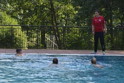 Schwimmtrainer beobachtet zwei Schwimmer im Wasser und einen weiteren am Beckenrand in einem Freibad.