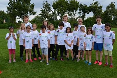 Gruppe von Kindern in weißen T-Shirts steht auf einer Wiese, umgeben von Bäumen, lächelnd für ein Gruppenfoto.