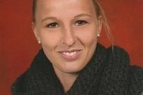 Portr&auml;t einer l&auml;chelnden Frau mit blonden Haaren, die einen schwarzen, grob gestrickten Schal tr&auml;gt. Hintergrund in Rot.