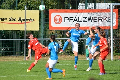 Spielszene im Frauenfu&szlig;ball: Spielerinnen springen um einen Ball, w&auml;hrend eine Gegnerin einen Schuss abwehrt.