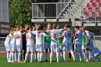 Frauenfu&szlig;ballmannschaft steht im Kreis und bespricht sich vor einem Spiel auf dem Rasenplatz.