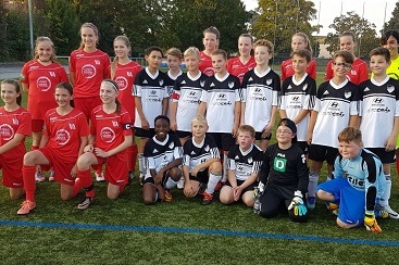 Gruppenfoto von zwei Jugendfu&szlig;ballmannschaften in roten und schwarzen Trikots auf einem Kunstrasenplatz.