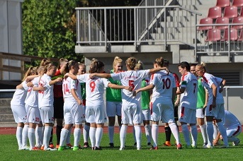 Frauenfu&szlig;ballmannschaft steht im Kreis und bespricht sich vor einem Spiel auf dem Rasenplatz.