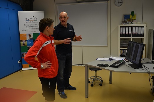 Zwei Personen im Gespr&auml;ch vor einem Computerbildschirm in einem modernen Raum mit Informationsmaterial im Hintergrund.