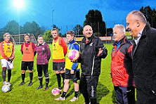 Sechs Fu&szlig;ballspielerinnen in Trikots mit zwei Erwachsenen auf einem Trainingsfeld bei D&auml;mmerung, jeder h&auml;lt einen Fu&szlig;ball.