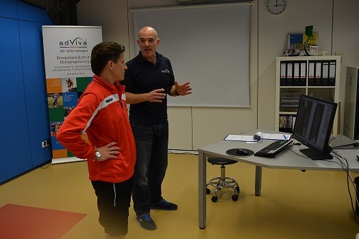 Zwei Personen im Gespr&auml;ch vor einem Computerbildschirm in einem modernen Raum mit Informationsmaterial im Hintergrund.