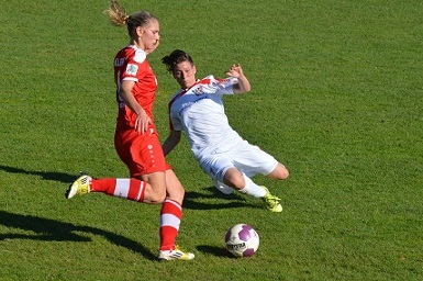 Zwei Fu&szlig;ballspielerinnen im Zweikampf; eine Spielerin liegt am Boden, die andere steht im roten Trikot.