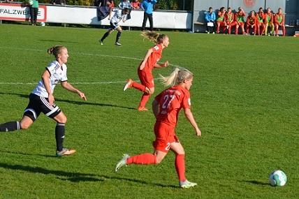 Zwei Fu&szlig;ballspielerinnen sprinten auf einem gr&uuml;nen Feld; eine Spielerin tr&auml;gt Rot, die andere Schwarz-Wei&szlig;.