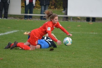 Zwei Fu&szlig;ballspielerinnen im Wettkampf; eine in roter, die andere in blauer Kleidung, geraten ins Fallen auf dem Rasen.