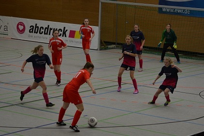 M&auml;dchenfu&szlig;ballspiel in einer Halle mit Spielerinnen in roten und blauen Trikots, die um einen Ball k&auml;mpfen.