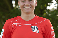 Portrait einer lächelnden Person in rotem Fußballtrikot vor grüner Hintergrundkulisse.