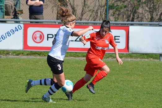Zwei Fu&szlig;ballspielerinnen auf dem Platz, eine in schwarz-wei&szlig;er, die andere in roter Spielkleidung, im Zweikampf um den Ball.