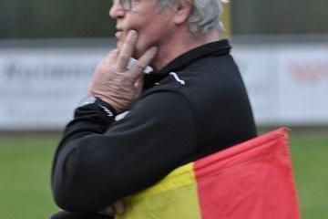 Ein Schiedsrichter mit grauen Haaren h&auml;lt eine rot-gelbe Fahne und denkt nach, w&auml;hrend er am Spielfeldrand steht.