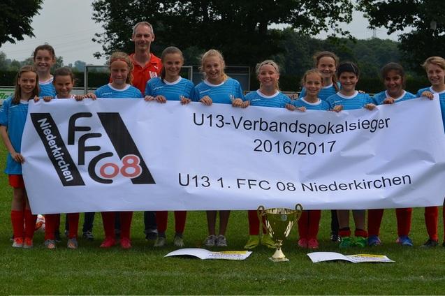 Eine M&auml;dchenfu&szlig;ballmannschaft steht mit einem Siegerbanner und einem Pokal auf einem gr&uuml;nen Spielfeld.