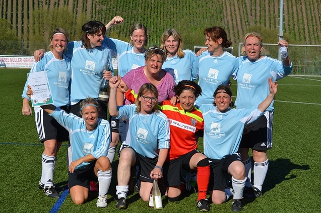 Gruppenselfie einer Frauenfu&szlig;ballmannschaft in blauen Trikots, die stolz Pokale und Urkunden pr&auml;sentieren.