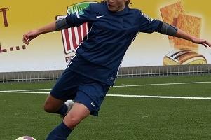 M&auml;dchen in blauer Fu&szlig;ballausr&uuml;stung tritt einen Ball auf einem Kunstrasenplatz.