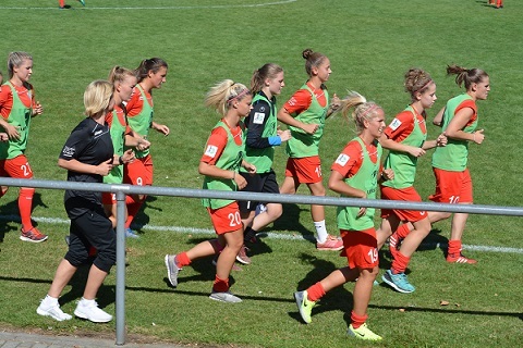 Mannschaft beim Aufw&auml;rmen auf dem Fu&szlig;ballplatz, getragen in gr&uuml;nen und roten Trikots.