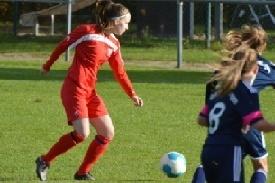 Junge Fu&szlig;ballspielerin in rotem Trikot dribbelt den Ball auf einem Rasenplatz, umgeben von anderen Spielerinnen.