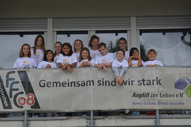 Gruppe von Jugendlichen und Kindern posiert auf einem Balkon vor einem Banner mit der Aufschrift &bdquo;Gemeinsam sind wir stark&ldquo;.