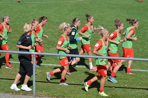 Mannschaft beim Aufw&auml;rmen auf dem Fu&szlig;ballplatz, getragen in gr&uuml;nen und roten Trikots.