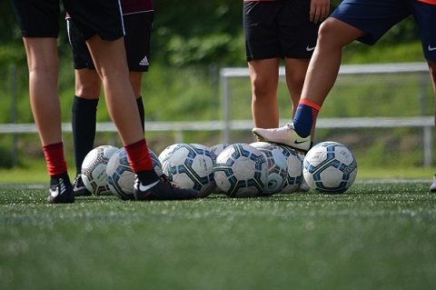 Fu&szlig;ballspieler stehen um mehrere Fu&szlig;b&auml;lle auf einem gr&uuml;nen Kunstrasenplatz.