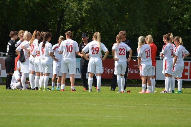 Frauenfu&szlig;ballmannschaft h&ouml;rt einem Trainer w&auml;hrend einer Besprechung auf dem Rasenplatz aufmerksam zu.