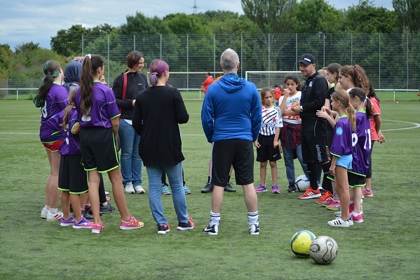 Gruppe von M&auml;dchen in Sportkleidung versammelt sich auf einem Fu&szlig;ballplatz zu einer Besprechung mit Trainern.
