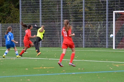 M&auml;dchenfu&szlig;ballspiel: Spielerinnen in roten und blauen Trikots, Ball fliegt auf das Tor zu, Torwart bereitet sich vor.