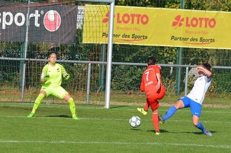 Spielszene: Eine Spielerin in roten Trikots schie&szlig;t auf das Tor, w&auml;hrend die Torh&uuml;terin in Gelb und eine Verteidigerin in Wei&szlig; reagieren.