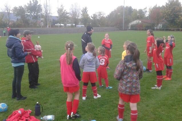 Gruppentraining eines M&auml;dchenteams auf einem Fu&szlig;ballplatz, Trainer spricht mit den Spielerinnen in roten Trikots.