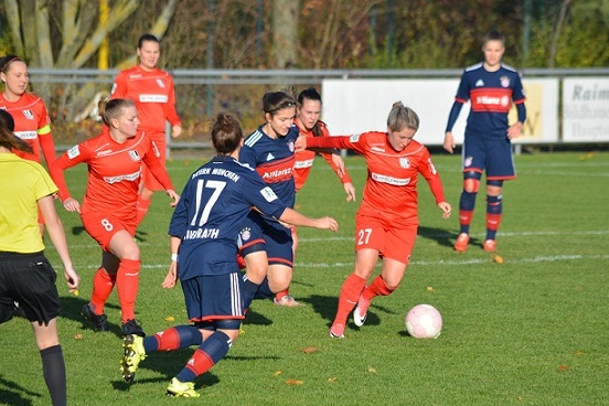 Sechs Frauenfu&szlig;ballspielerinnen auf dem Feld k&auml;mpfen um den Ball, w&auml;hrend eine Schiedsrichterin das Spiel leitet.