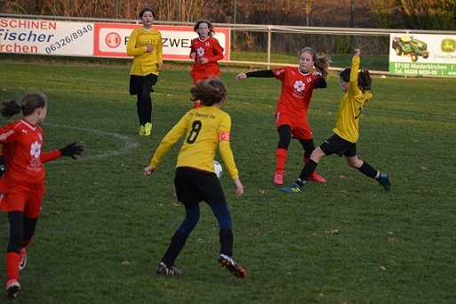 M&auml;dchenfu&szlig;ballspiel auf dem Feld, Spielerinnen in roten und gelben Trikots k&auml;mpfen um den Ball.