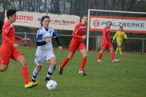 Vier Fu&szlig;ballspielerinnen auf dem Platz, eine in Wei&szlig; dribbelt den Ball, w&auml;hrend andere in Rot versuchen, zu verteidigen.