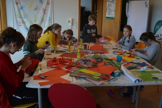 Gruppe von Kindern, die an einem Tisch mit farbigem Bastelmaterial und Werkzeugen kreativ arbeiten.
