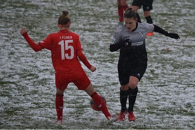 Zwei Fu&szlig;ballspielerinnen im Schneetreiben, eine in rotem Trikot mit der Nummer 15 und eine in grauem Trikot, im Wettkampf.