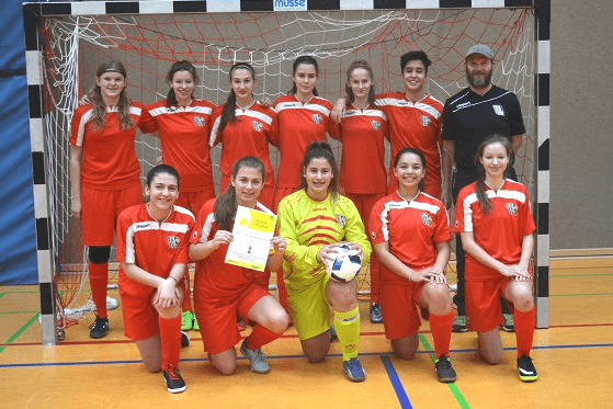 Gruppe von Fu&szlig;ballspielern in roten Trikots, zusammen mit einem Torwart in Gelb, vor einem Toreing.